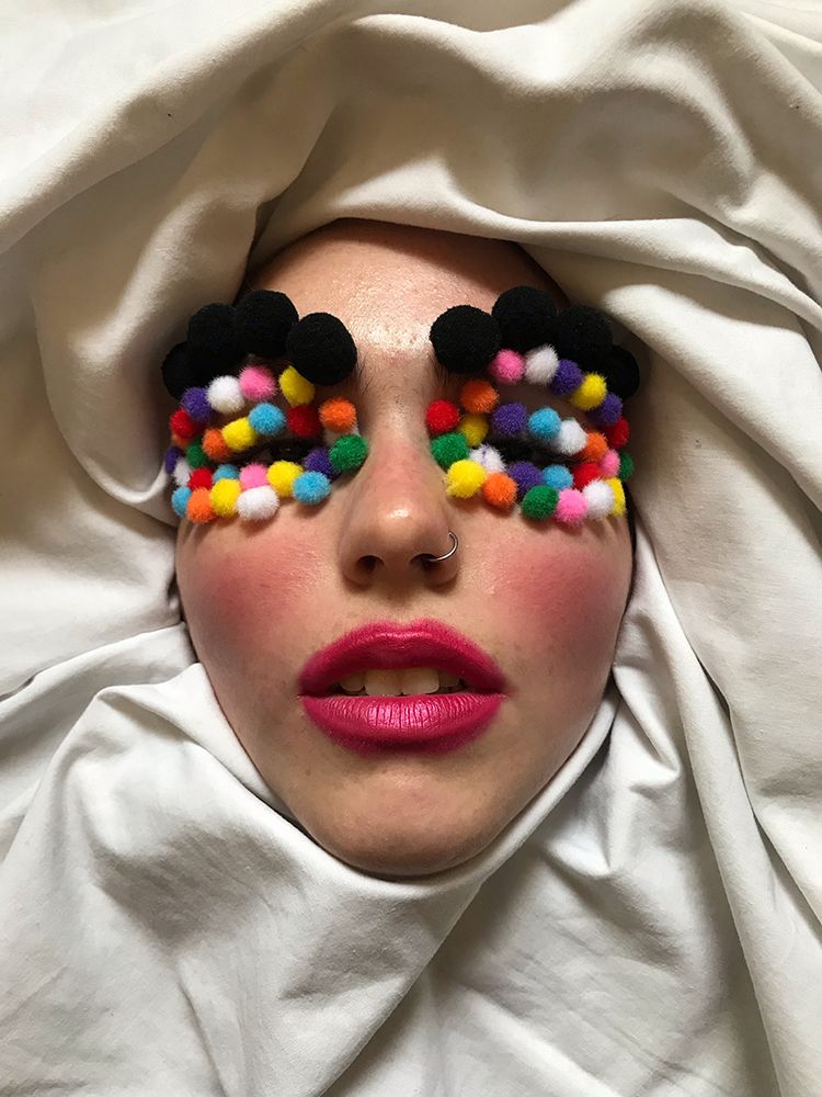 Close up of female model with multicoloured pom poms on eyelids and pink lipstick