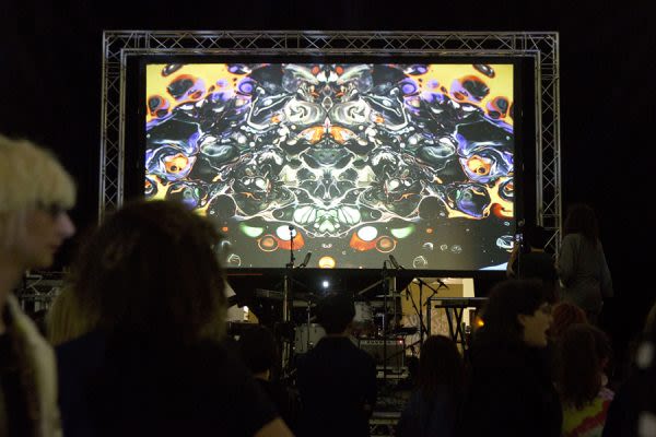 Photograph of a large screen above a stage showing a digital abstract graphic 