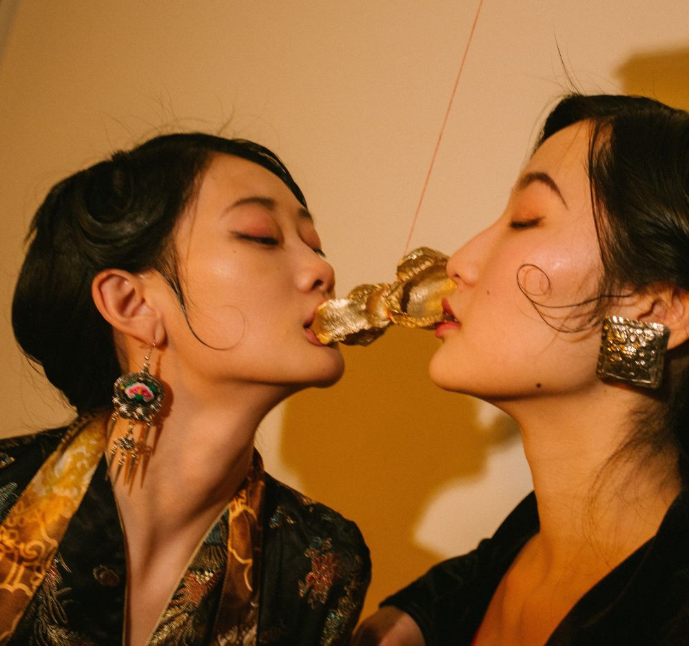 Two female asian models kissing with gold souldered metal between their mouths