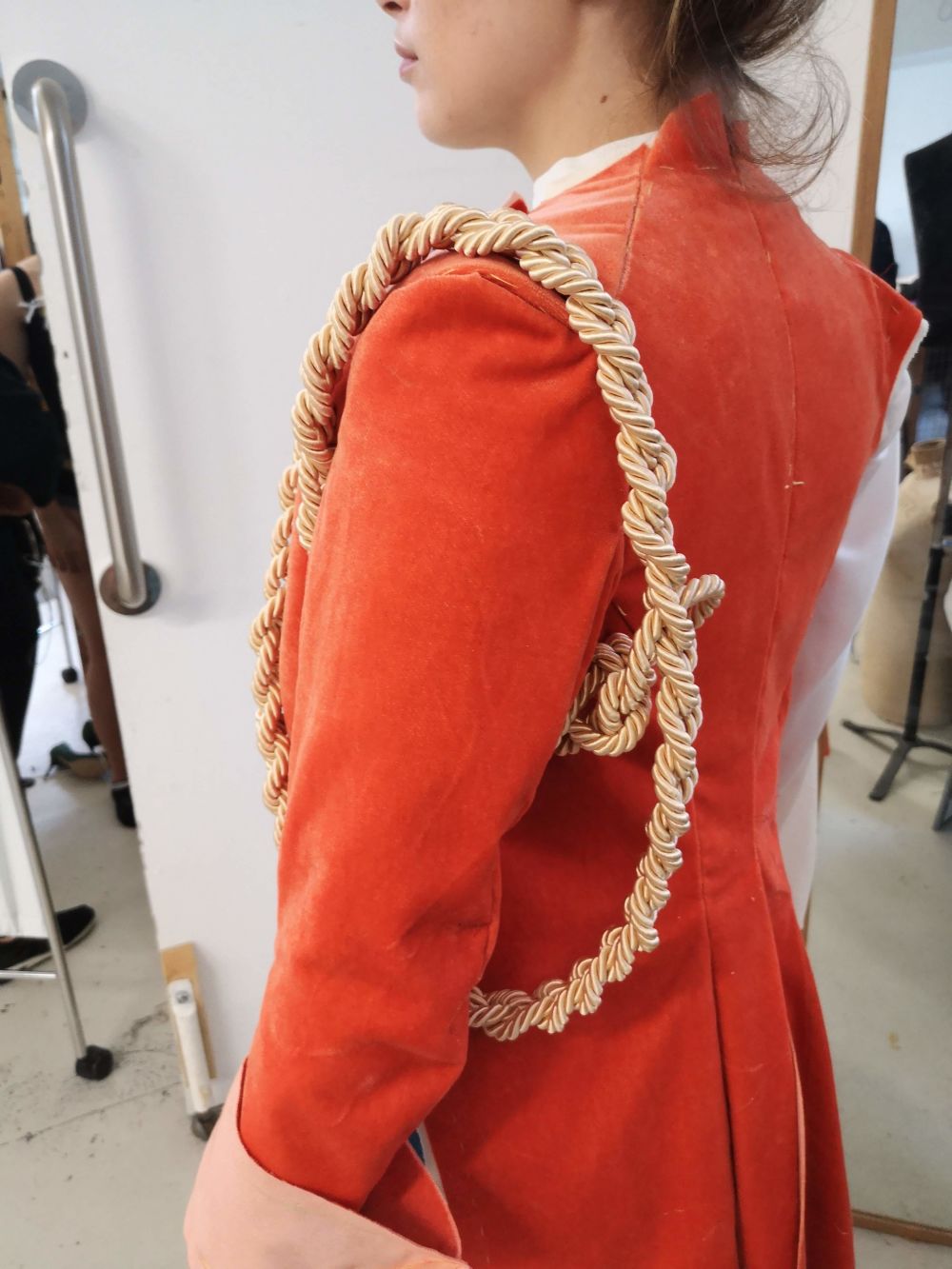Photo of a person wearing a red velvet coat, with gold rope around the arm. Photo taken from the left side