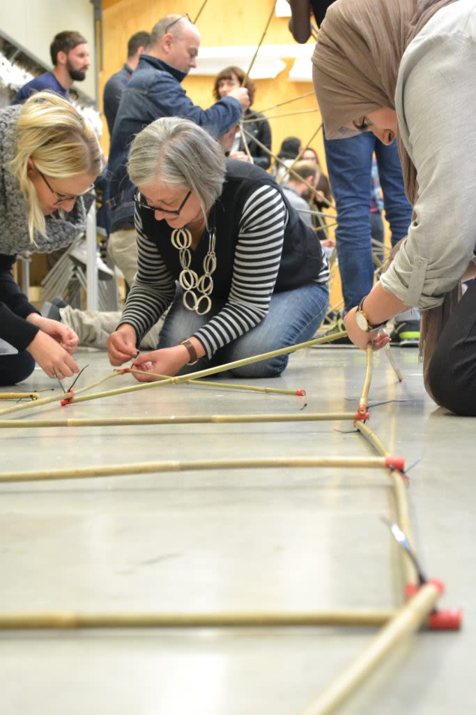 Three participants work closely on constructing the structure on the floor.