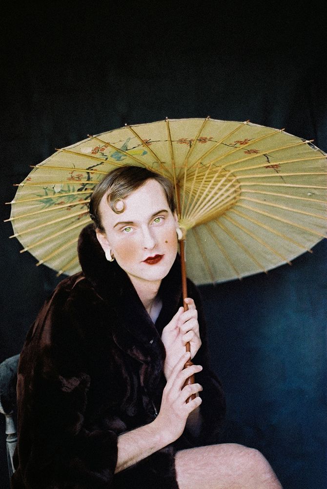 Photograph of male model wearing a fur coat and lipstick holding a parasol