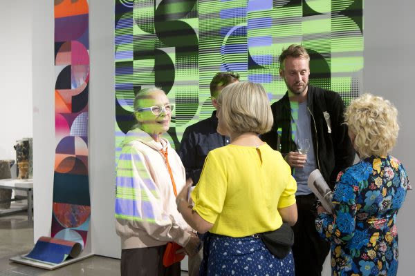 Photograph of people stood in the gallery talking to each other next to the artwork