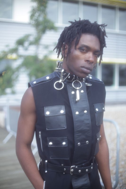 Male model with dreadlocks wearing a black vest with leather panels and silver chain necklace
