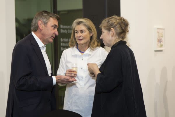 Three people photographed mid conversation in a gallery 