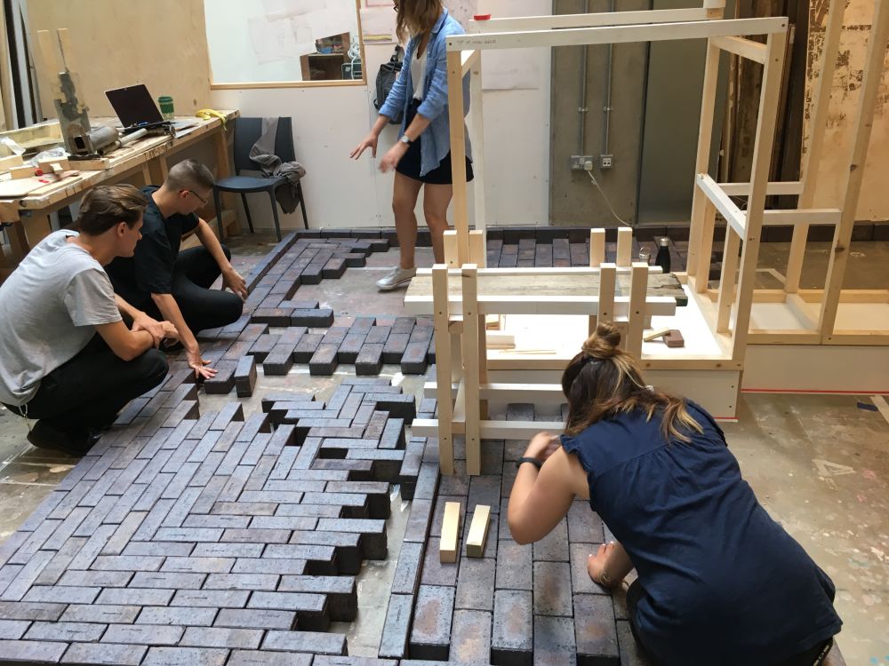 People arranging bricks in pattern on floor