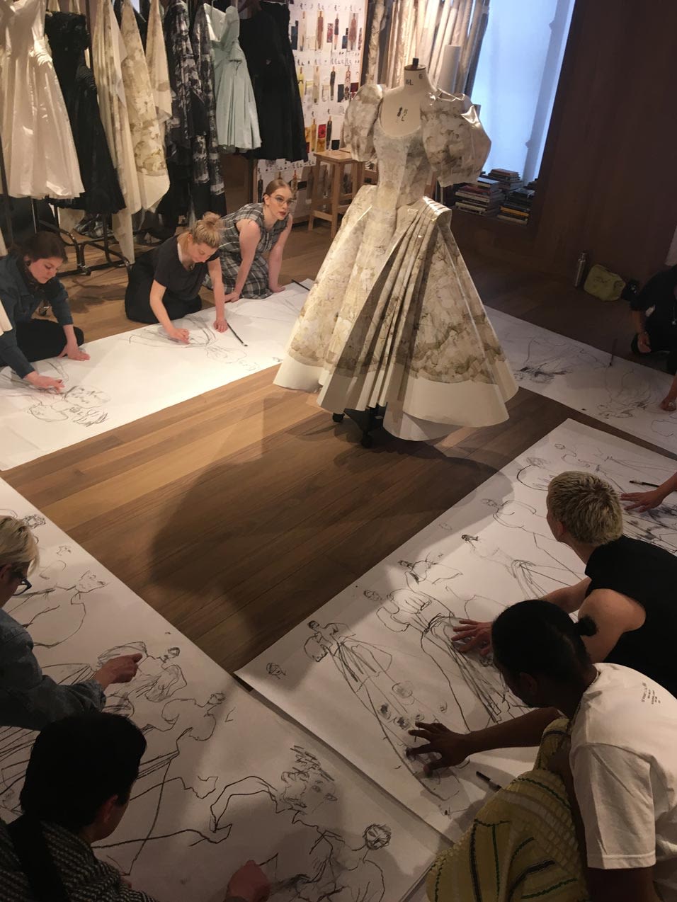 People sitting sketching around dress on stand