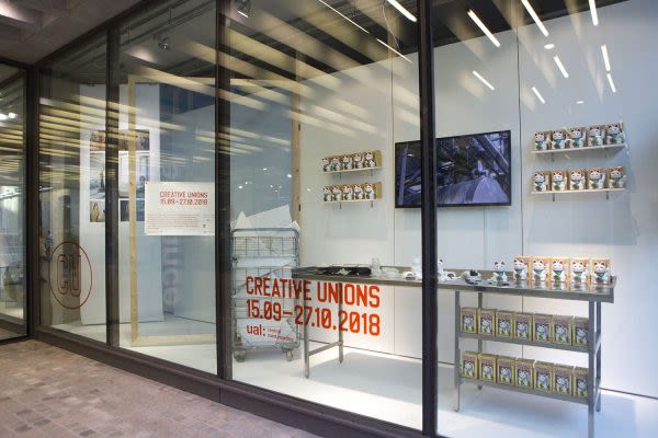 Photograph of the window gallery from outside, showing the installed exhibition through the glass, which is made up of a television mounted at the back and a table displaying objects