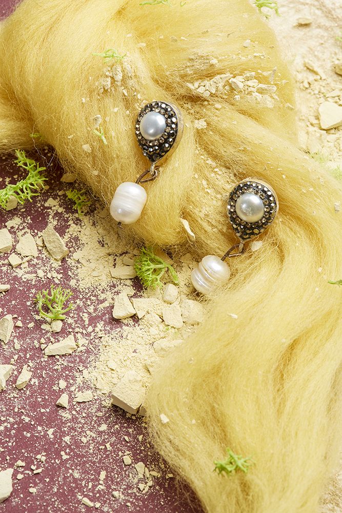 Work by Visual Merchandising - Interiors students, taken by Sarah Manning. Pearl earrings pinned to a yellow hair like material with scattered crushed concrete below.