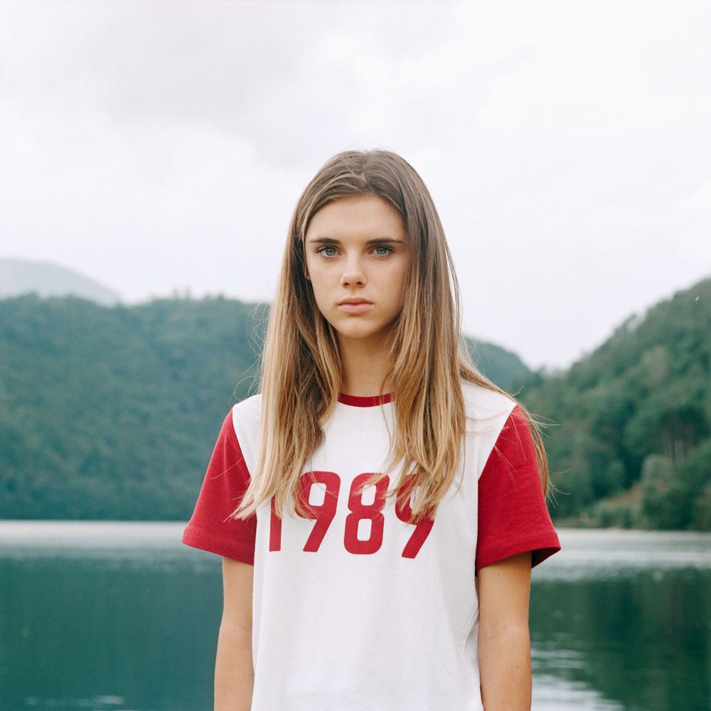 Portrait of adolescent girl with long blonde hair and a t-shirt with slogan '1989' in front of a picturesque lake