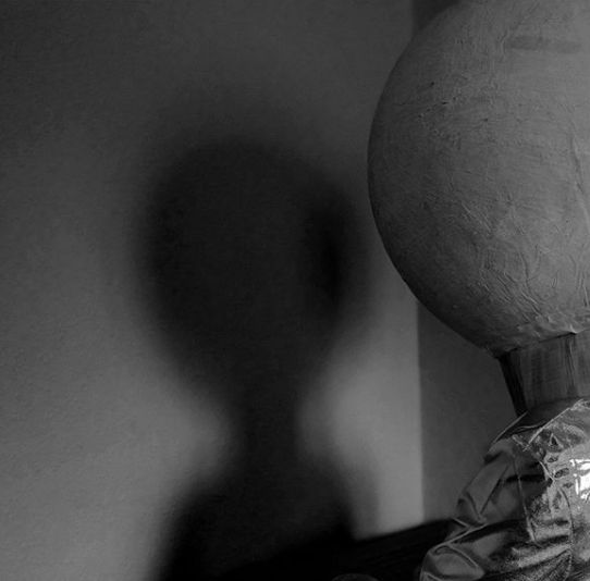 black and white photo of person with large ball on head standing in front of white wall - shadow play