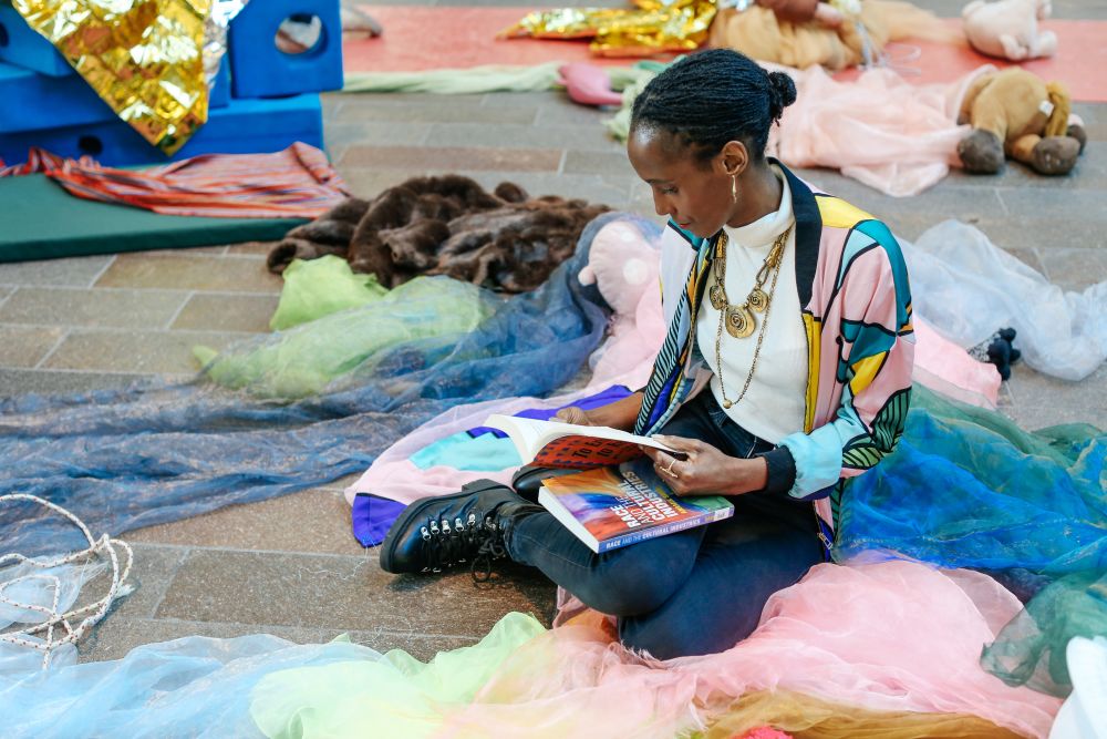 Rochelle Saunders reading a book among fabrics and creative materials.