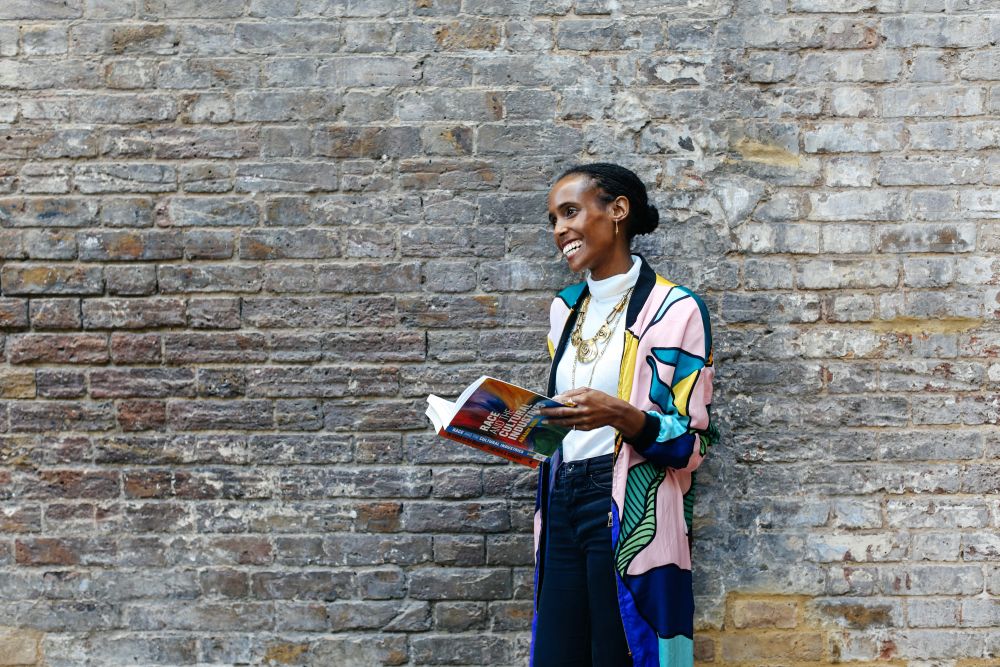 Rochelle Saunders standing in front of a brick wall holding a book and laughing.