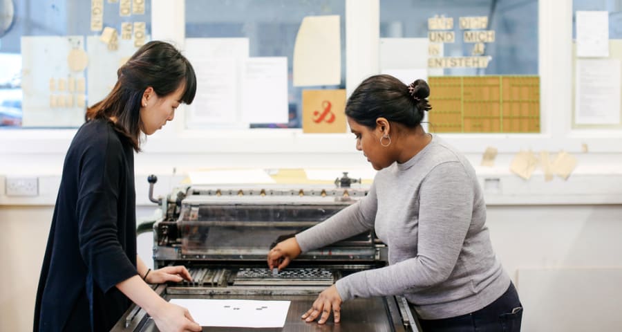 Two woman are stood at a letterpress machine.