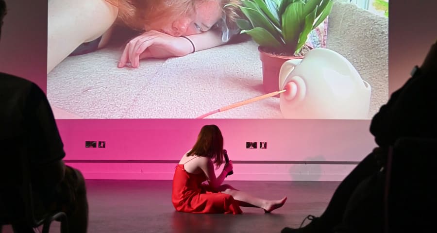 Girl sits on stage with a microphone looking away from audience at a photo projected on the wall