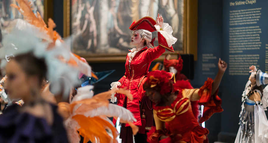 A woman dressed in a red dress and hat waving her hand in the air